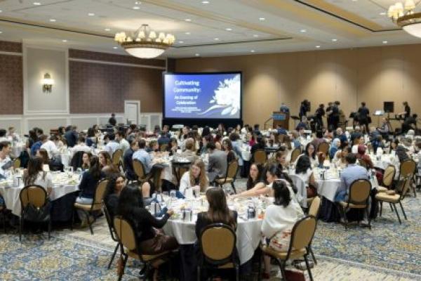Students, faculty, staff and community partners sit at round banquet tables during the OHACE year-end celebration at Hershey Lodge, facing a stage with a screen displaying the words “Cultivating Community: An Evening of Celebration.”