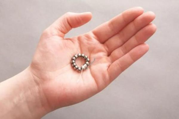 A hand holding the LINX device, a small band of magnetic titanium beads