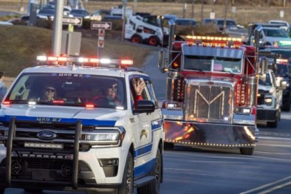 A line of vehicles with flashing lights drives toward the camera. They include emergency vehicles, tow trucks and others.