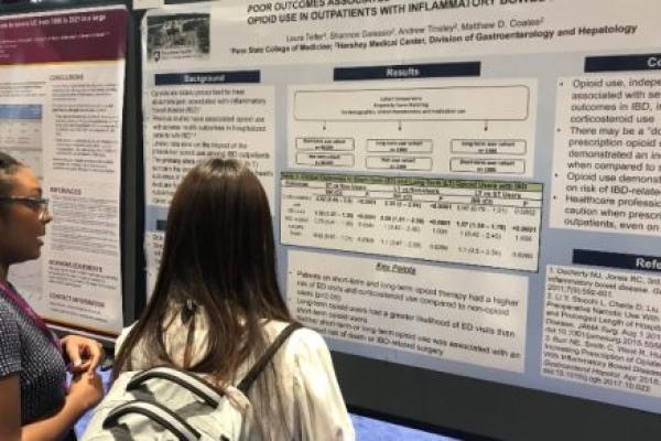 Laura Telfer, a third-year medical student, stands in the foreground with a poster in the background that summarizes a research project and explains the project to another individual looking on during Digestive Disease Week in Chicago, Illinois.