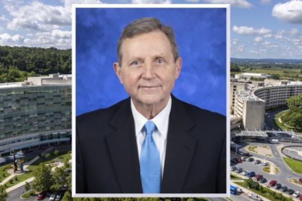 A professional headshot photo of Dr. Robert Harbaugh wearing a suit and tie is superimposed over an image of Milton S. Hershey Medical Center.