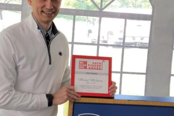 Dr. Michael McShane holds a framed award while standing at a podium.