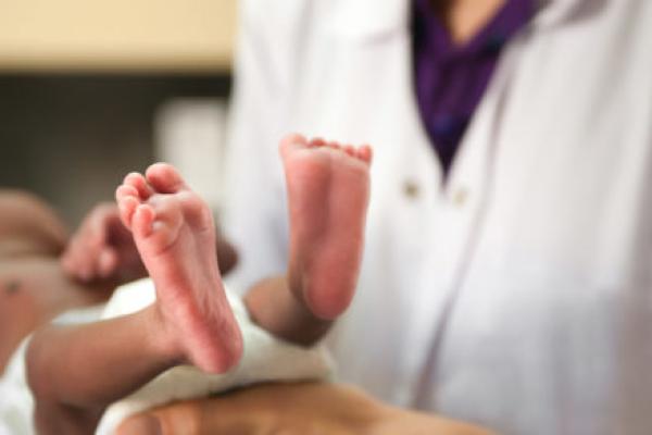 Photo of a doctor holding a newborn baby in a diaper, with the photo focusing on a close up of the baby’s feet.