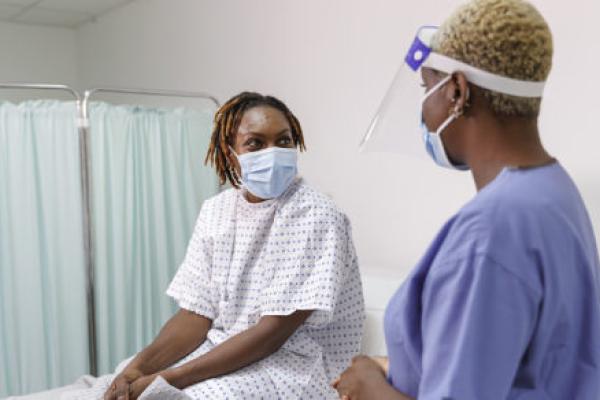 A Black, female patient discusses her care with a Black, female nurse. Both women are wearing masks.
