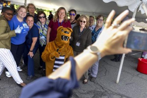 A group of about 10 people pose for a photo with the Penn State Nittany Lion underneath an outdoor event tent.