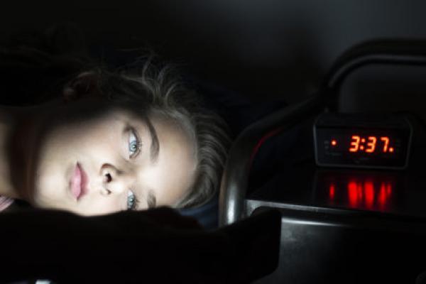 A young girl looks at her phone while laying awake at 3:37 AM unable to sleep.