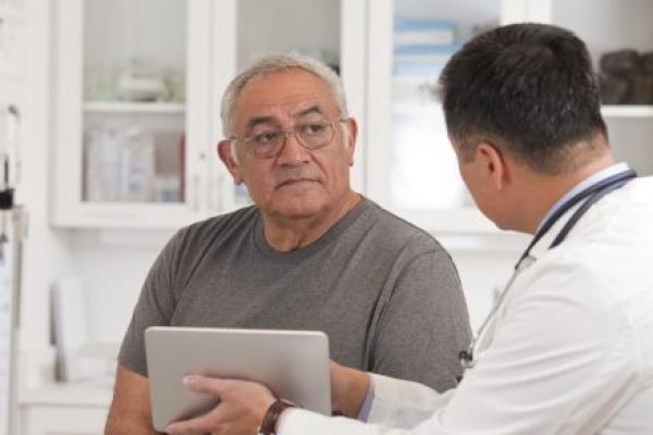 A doctor holds a digital tablet as he talks with a man.