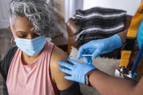 A Black nurse gives a COVID-19 vaccine to a senior Black woman.