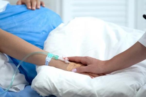 A doctor holds the hand of a pregnant woman in a hospital bed.