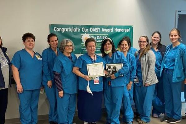 A group of women, most in hospital scrubs, pose for a photo. Two in the center hold plaques.