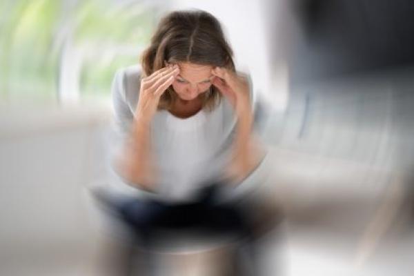 Woman sits looking down with puts her hands on her forehead. Circular lines around her indicate that she has vertigo.
