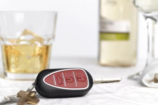 A set of car keys sits among glasses filled with alcohol on a white table cloth.