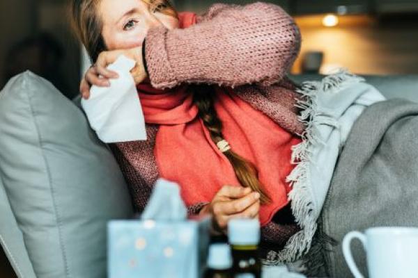 Woman coughing on a sofa and holding a tissue while sick with the flu.