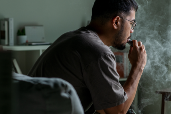 An individual sitting on a couch uses an e-cigarette.