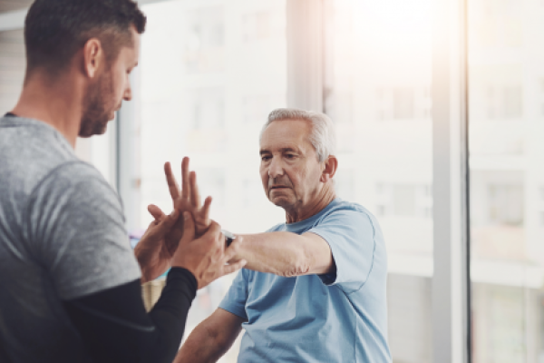 Older man doing hand therapy exercises with a physical therapist