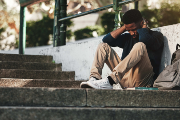 Young man with head bowed and sitting against a staircase.