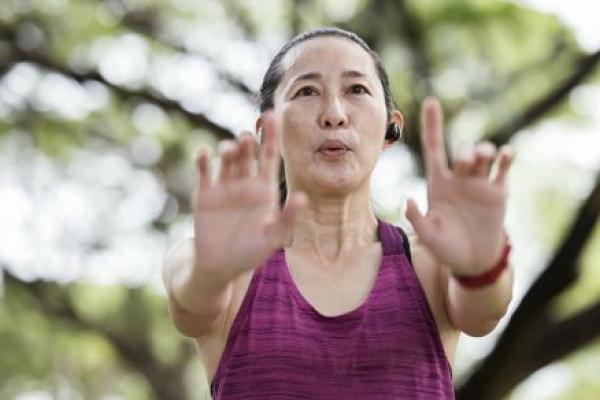 A woman practices qigong poses in a park.