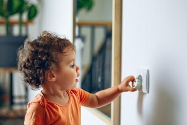 Toddler reaches into electrical outlet on wall with her hand.
