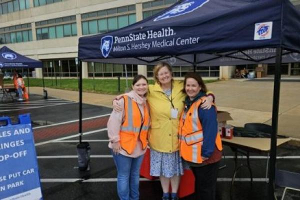 Two canopies branded Penn State Health Milton S. Hershey Medical Center are set up along the road in front of the medical center. Hospital staff stand under and around the canopies, facing the road.
