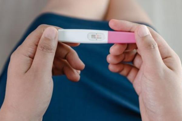 Close-up of a woman’s hands holding a pregnancy test kit and waiting for positive result in her bedroom.