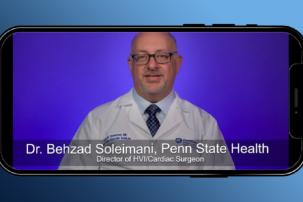 Dr. Bahzad Soleimani, Heart and Vascular Institute director and cardiac surgeon, talks during a video on a cell phone. He is wearing a white coat with his name and Penn State Heart and Vascular Institute on the left and the Hershey Medical Center logo on the right. A graphic identifies him as Dr. Bahzad Soleimani, Penn State Health, Director of HVI/Cardiac Surgeon.
