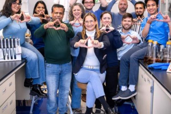 Ten people in a lab pose for a photo shaping their fingers into a triangle