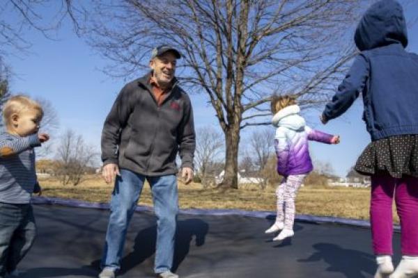 Man jumps on trampoline with three young grandchildren.