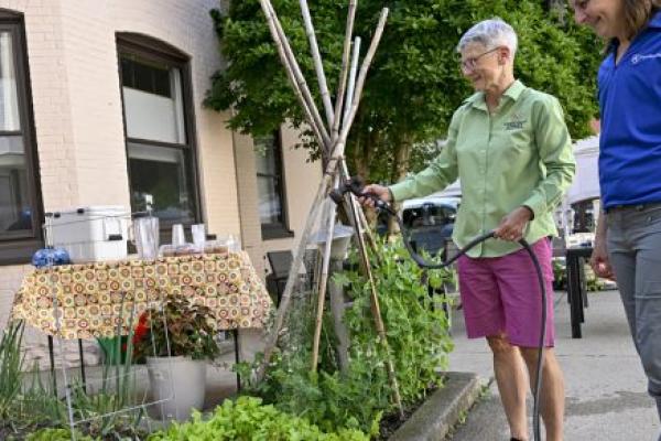 Laurie Funk, left, director of the Chestnut Street Community Center in Lebanon, holds a hose and waters a garden filled with lettuce and other produce. Laurie Crawford, Penn State Health program manager for food access, stands next to her.