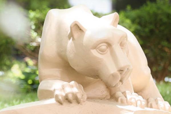 A statue depicting the mascot of Penn State University, the Nittany Lion, surrounded by bushes.
