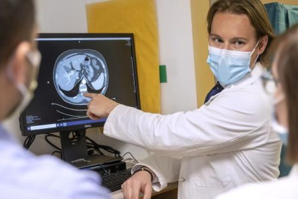 Dr. Jonathan Stine, center, points to a CT scan image as he looks at two people in the Fatty Liver Disease Program. He is wearing a mask and a white coat.