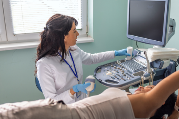 Healthcare provider in a medical exam room performing breast ultrasound exam on a woman.