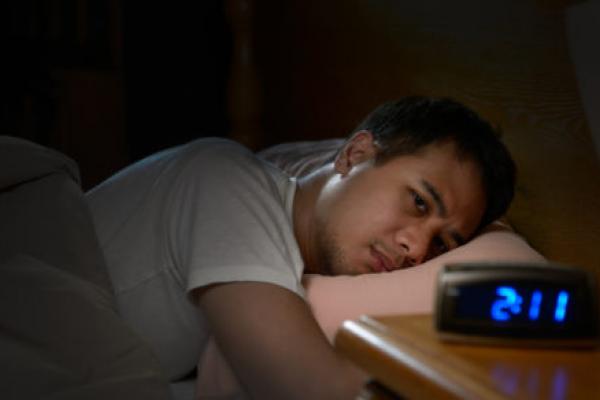 Man lays awake in bed looking at a clock
