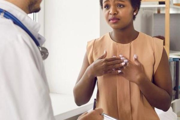 A patient sitting in a medical exam room, speaking earnestly with a doctor who is taking notes on a clipboard.