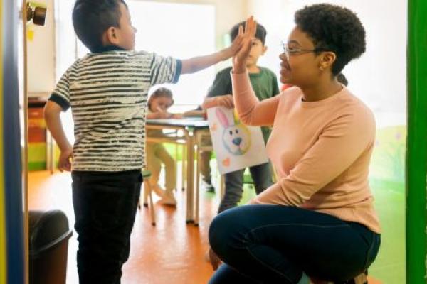 Happy African American preschool teacher high fiving a student entering the classroom - back to school concepts