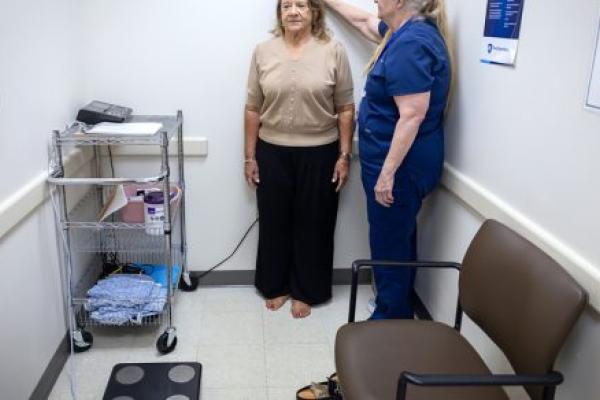 A woman gets her height measured by a medical assistant in a doctor’s office.