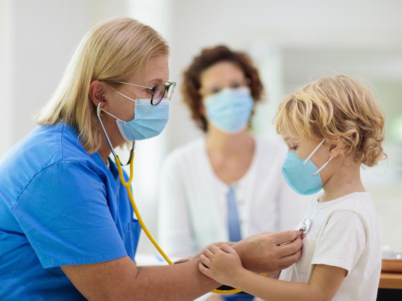 A nurse checks a child's heartbeat with a stethoscope while a guardian looks on.