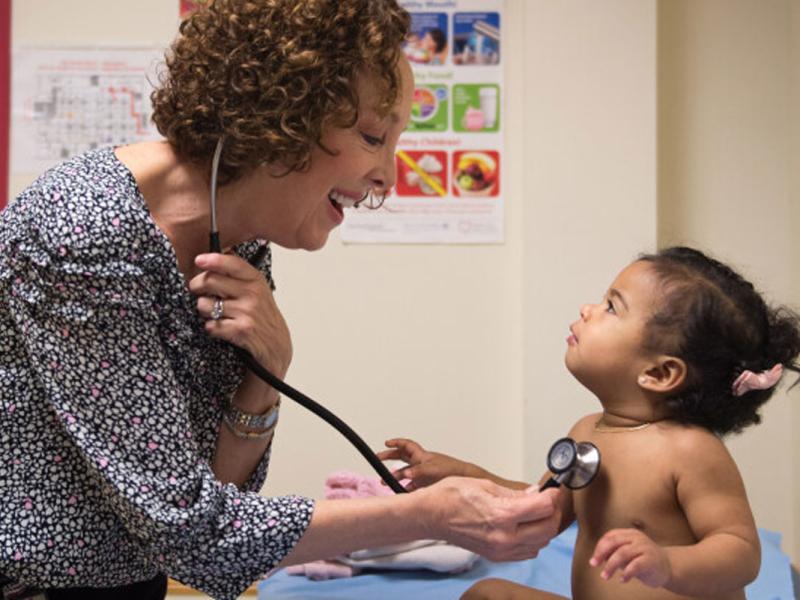Female practitioner with stethoscope on infants chest listening to heart.