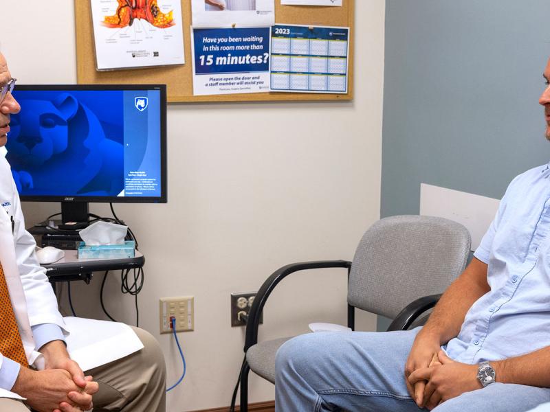 Male doctor sitting in an exam room speaking with a male patient.
