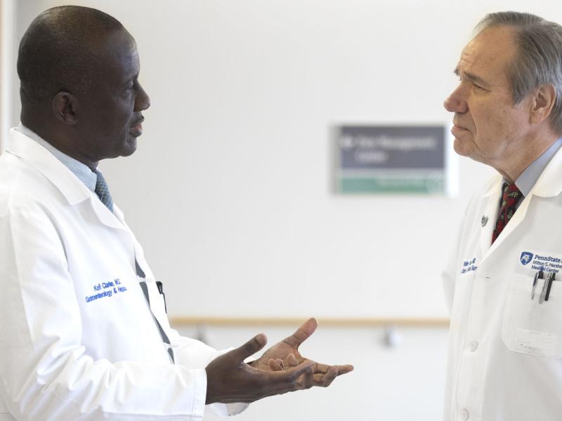 Two male doctors in white lab coats engaged in a conversation in a hallway.