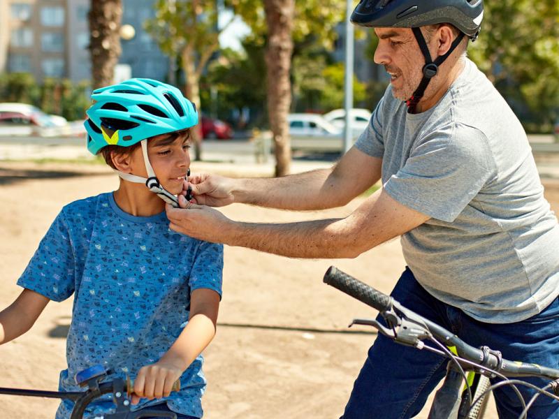 A father fastens the chin strap of his son’s bike helmet.