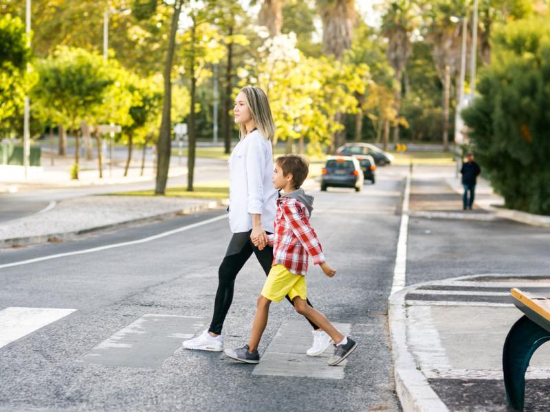 Young boy and mom holding hands and walking on the street crossroad.