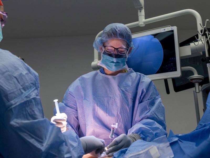 Two surgeons operate on a patient under light booms.
