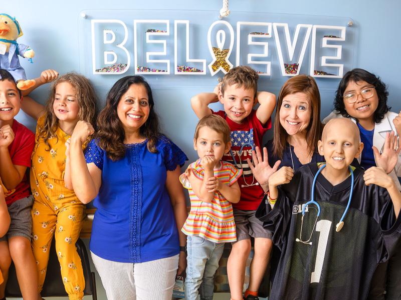 A group of young individuals and adults standing in front of a sign that says believe.