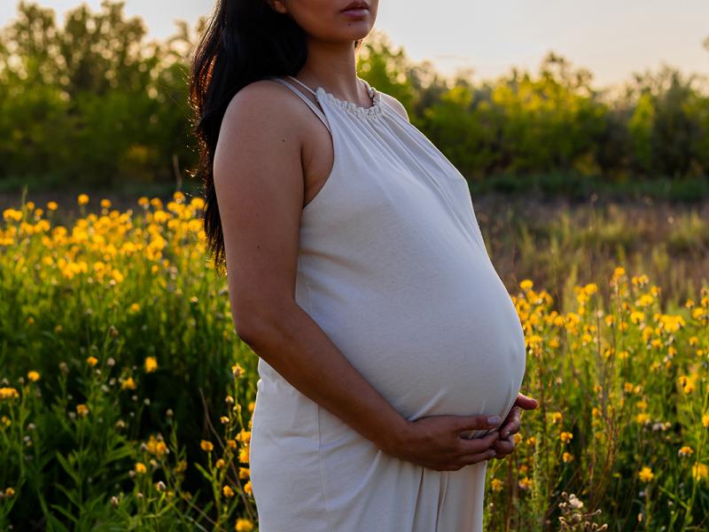 Pregnant woman holds belly outside in nature at sunset.