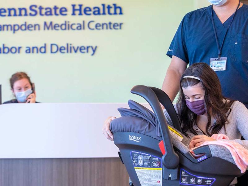 Young mother being wheeled out of labor and delivery unit with young baby in a car seat facing her.