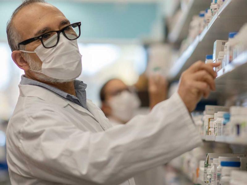 Pharmacist working at a pharmacy organizing products while wearing a protective face mask during the coronavirus outbreak.
