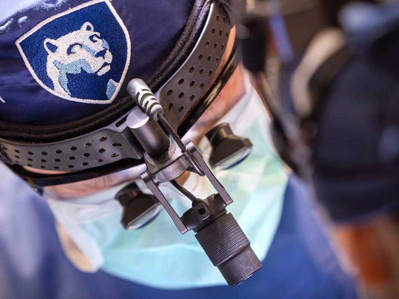 Medical professional wearing a surgical mask and magnifying loupes with a mounted light in a clinical setting.