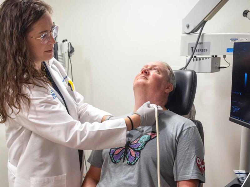 Penn State Health clinician using an ultrasound probe on a seated patient’s neck while viewing the scan on a nearby monitor.