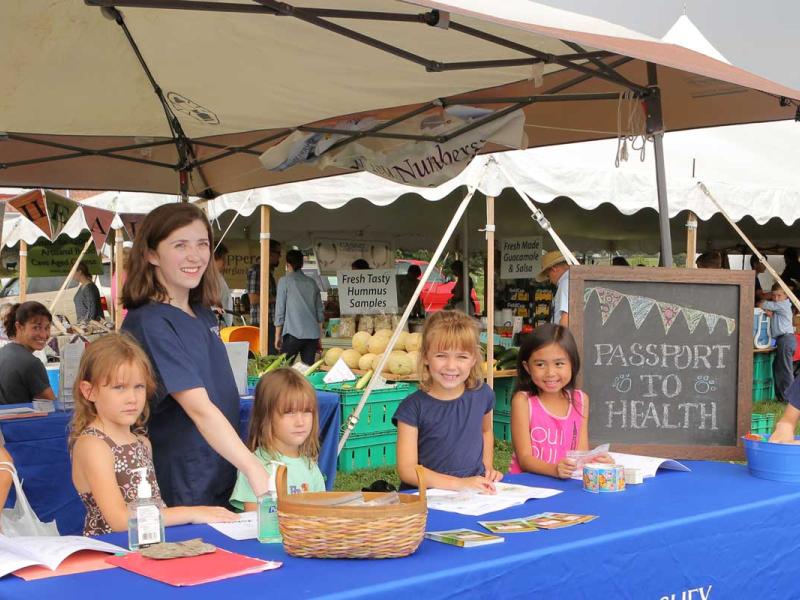 A group of children standing behind a table at a farmer's market.