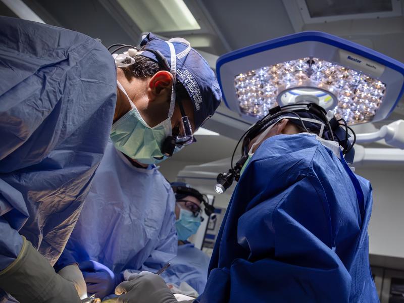 Three clinicians are looking down at something, probably on an operating table.